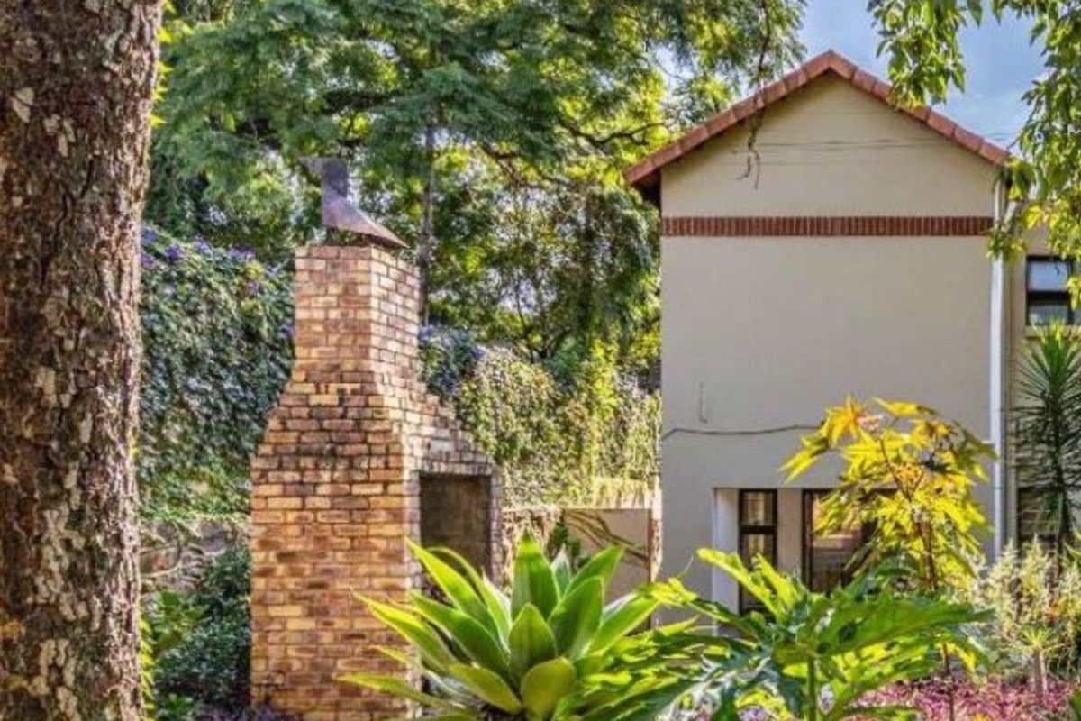 A view of the rear garden featuring a built-in brick fireplace and a well-maintained exterior facade with mature landscaping.
