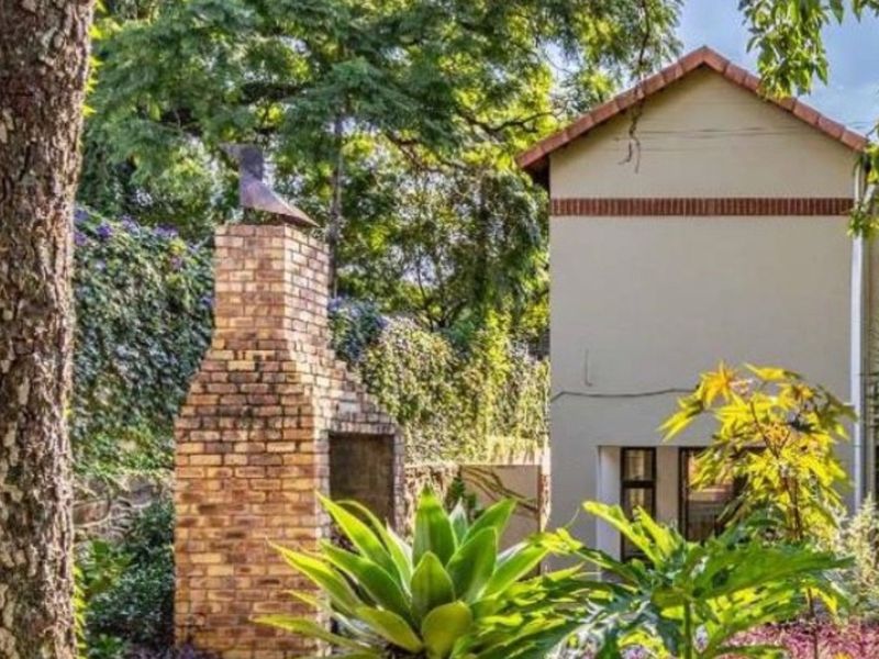 A view of the rear garden featuring a built-in brick fireplace and a well-maintained exterior facade with mature landscaping.