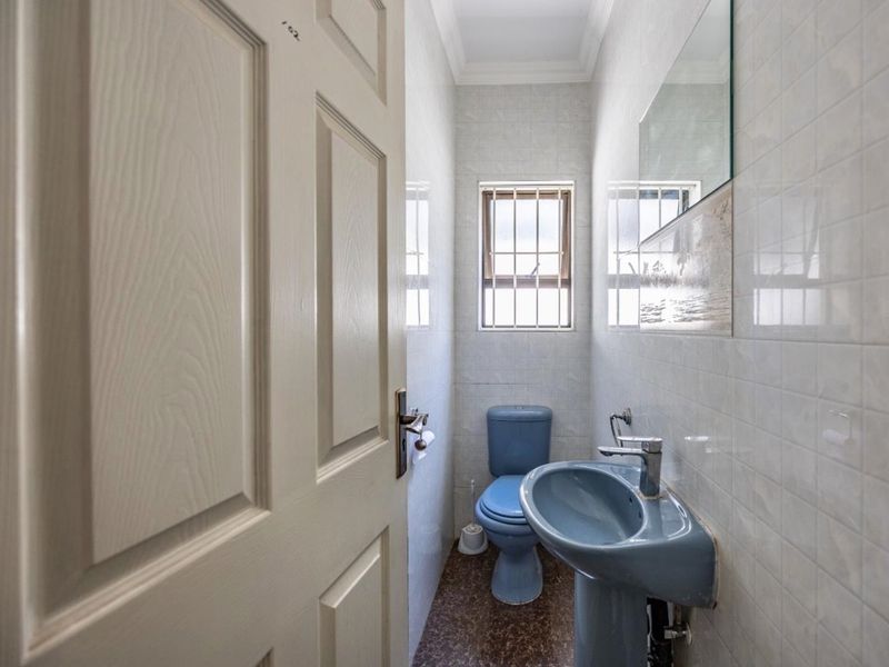 A compact guest bathroom featuring dated blue sanitaryware, tiled walls, and a small window with security bars.