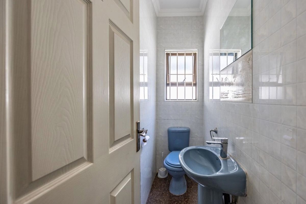 A compact guest bathroom featuring dated blue sanitaryware, tiled walls, and a small window with security bars.