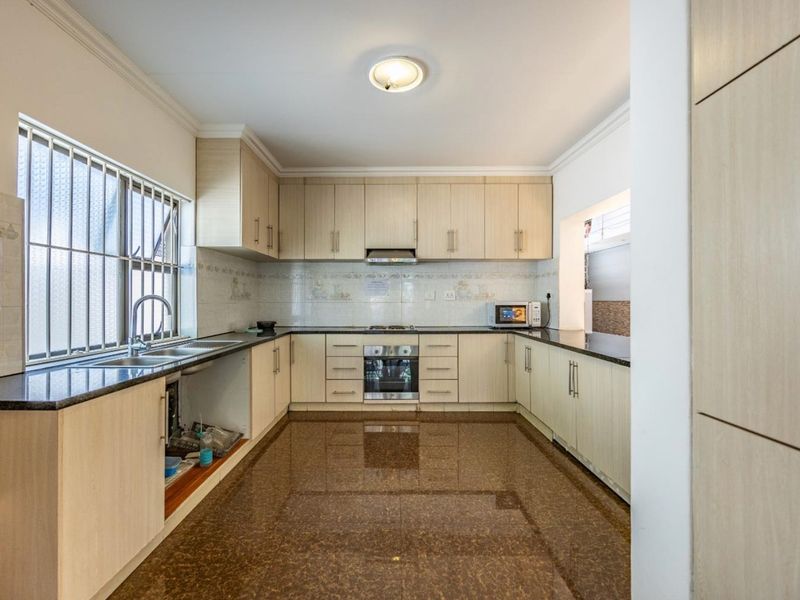 A functional kitchen featuring light wood cabinetry, granite countertops, built-in oven, gas hob, and tiled flooring, offering a clean and well-maintained workspace.