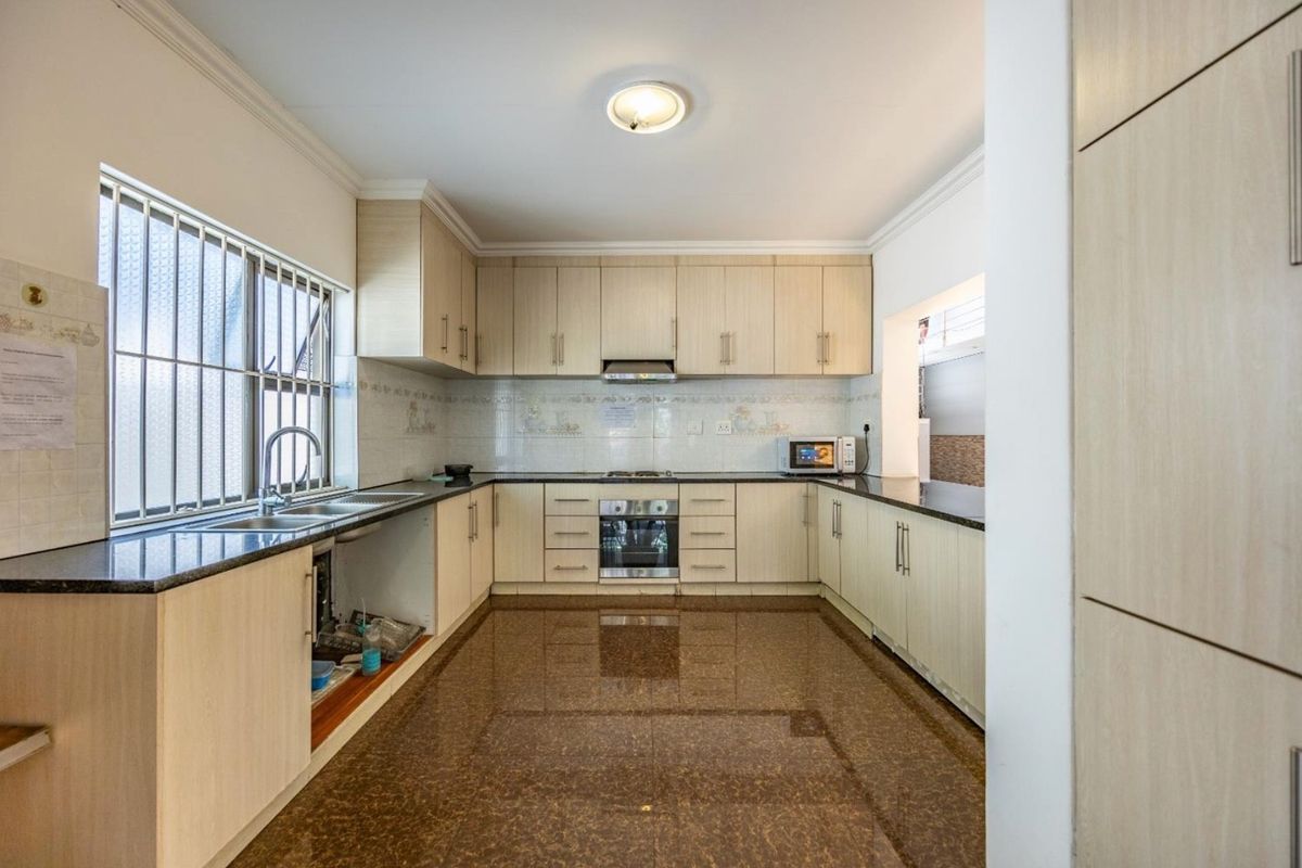A functional kitchen featuring light wood cabinetry, granite countertops, built-in oven, gas hob, and tiled flooring, offering a clean and well-maintained workspace.