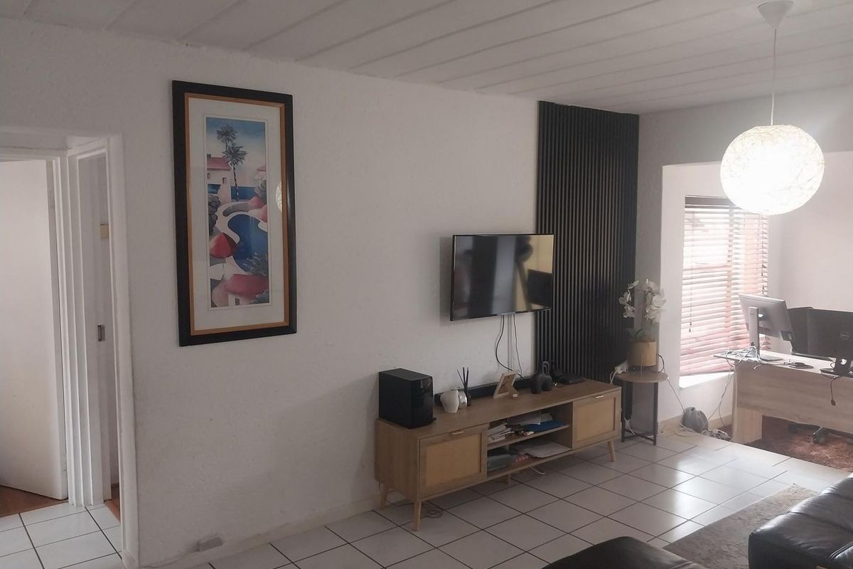 A living room featuring tiled flooring, a decorative slatted wood wall accent, and natural light through venetian blinds.