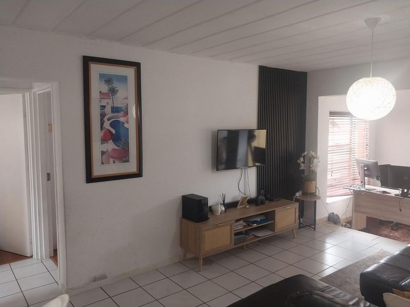 A living room featuring tiled flooring, a decorative slatted wood wall accent, and natural light through venetian blinds.