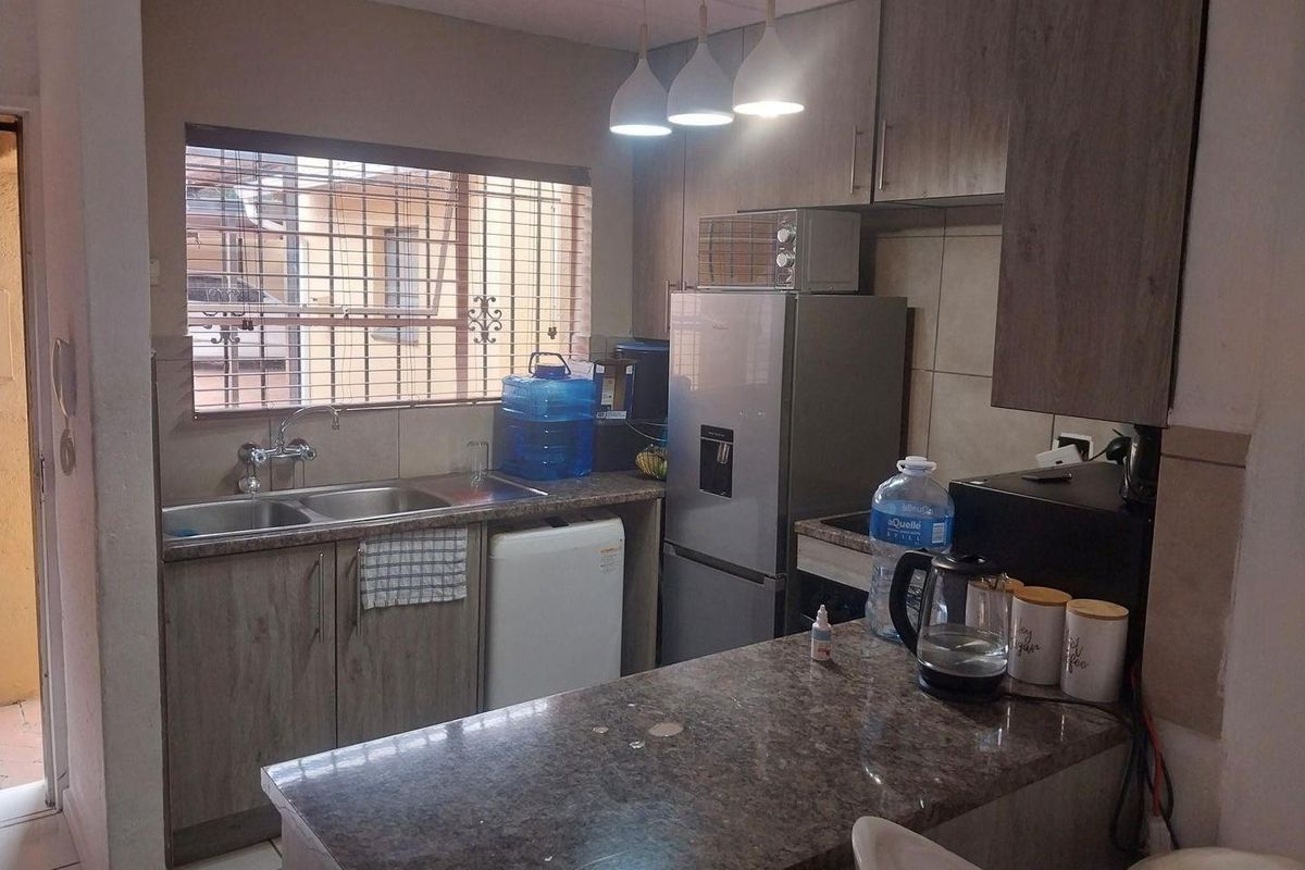 Compact kitchen featuring laminate cabinetry, stone countertops, a breakfast bar, and a double basin sink with security bars on the window.