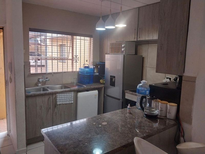 Compact kitchen featuring laminate cabinetry, stone countertops, a breakfast bar, and a double basin sink with security bars on the window.