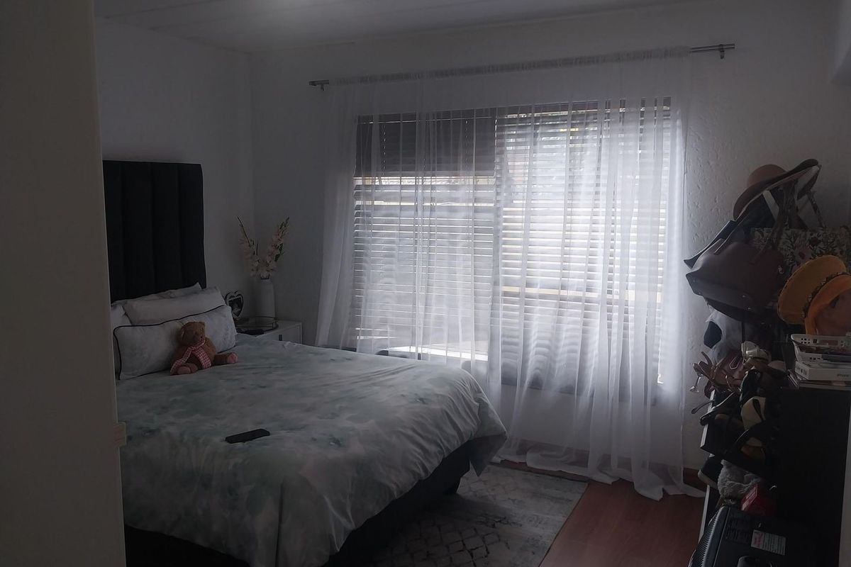 A bedroom featuring laminate flooring and window treatments including venetian blinds and sheer curtains.