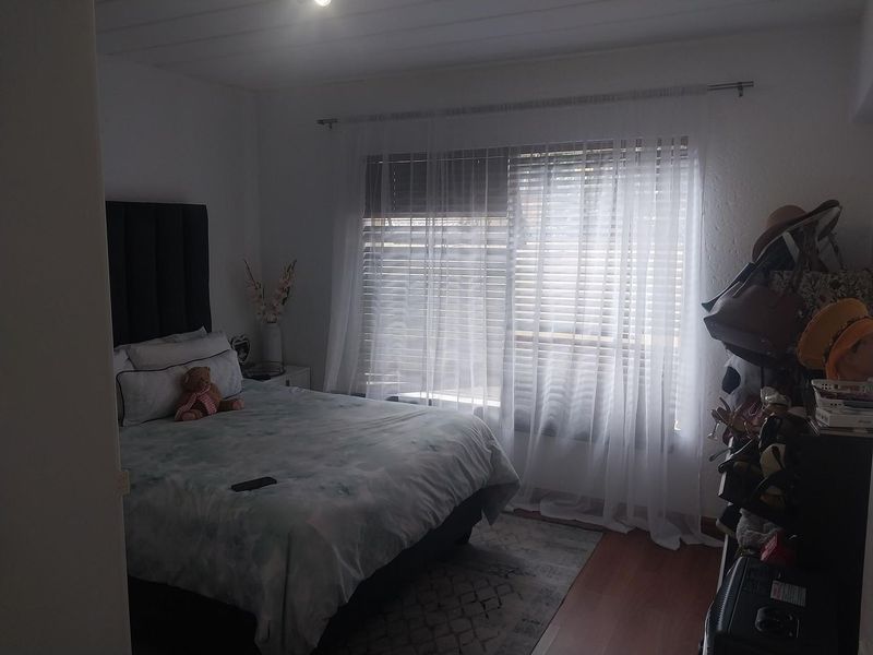 A bedroom featuring laminate flooring and window treatments including venetian blinds and sheer curtains.