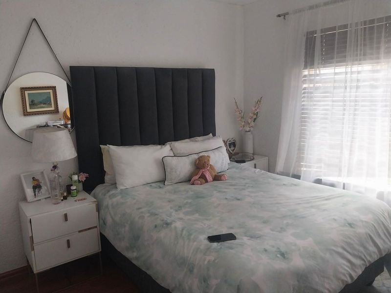A cozy bedroom featuring a dark upholstered headboard, neutral wall finishes, and window treatments including venetian blinds and sheer curtains.