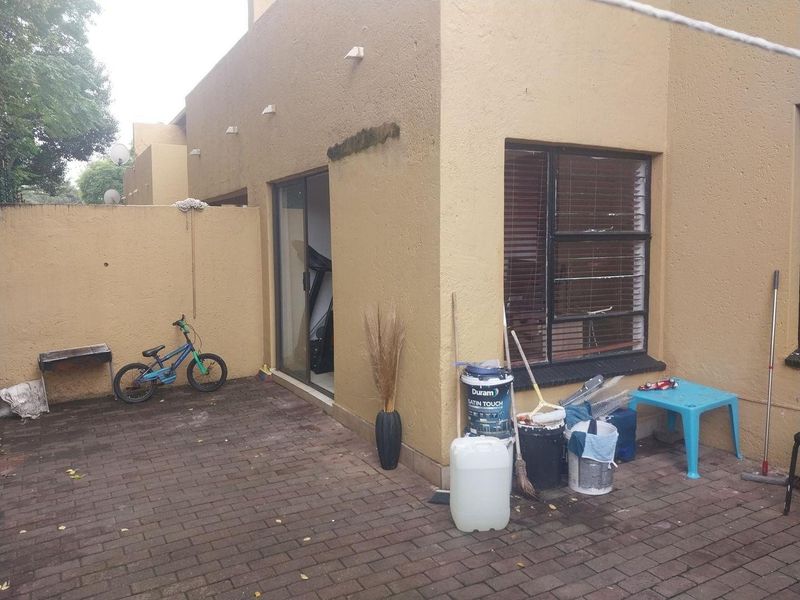 Rear exterior view of the apartment featuring a paved patio area, sliding glass door access, and window with fitted blinds.