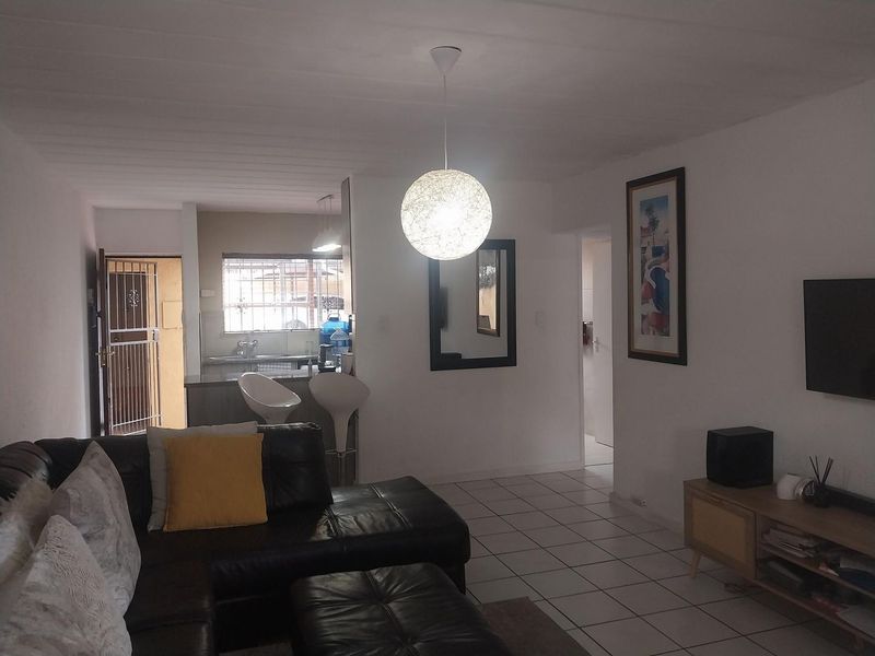 Open-plan living area featuring tiled flooring, a connected kitchen space, and a security gate at the entrance.