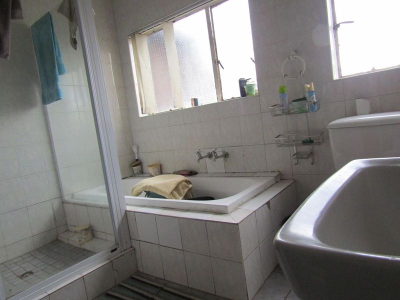 A dated bathroom featuring a built-in bathtub, separate shower enclosure, toilet, and washbasin with original ceramic wall tiling.