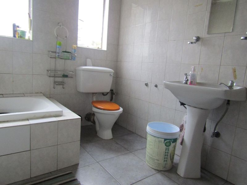 A dated bathroom featuring a pedestal basin, ceramic toilet, and a built-in bathtub with full-height wall tiling.