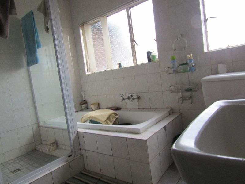 A dated bathroom featuring a built-in bathtub, separate shower enclosure, toilet, and washbasin with tiled finishes throughout.