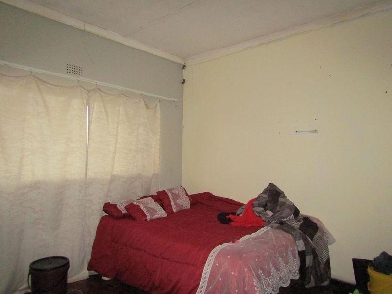 A bedroom featuring a ventilation grille and standard ceiling cornice, currently showing signs of wear on the walls and ceiling.