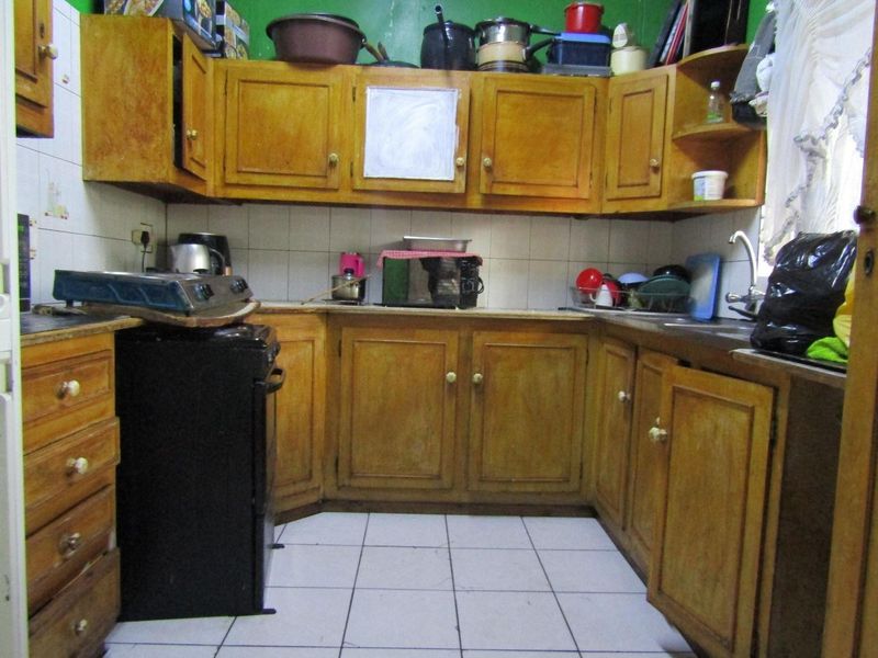 A dated kitchen featuring wooden cabinetry, tiled backsplash, and tiled flooring, offering potential for modernization and renovation.
