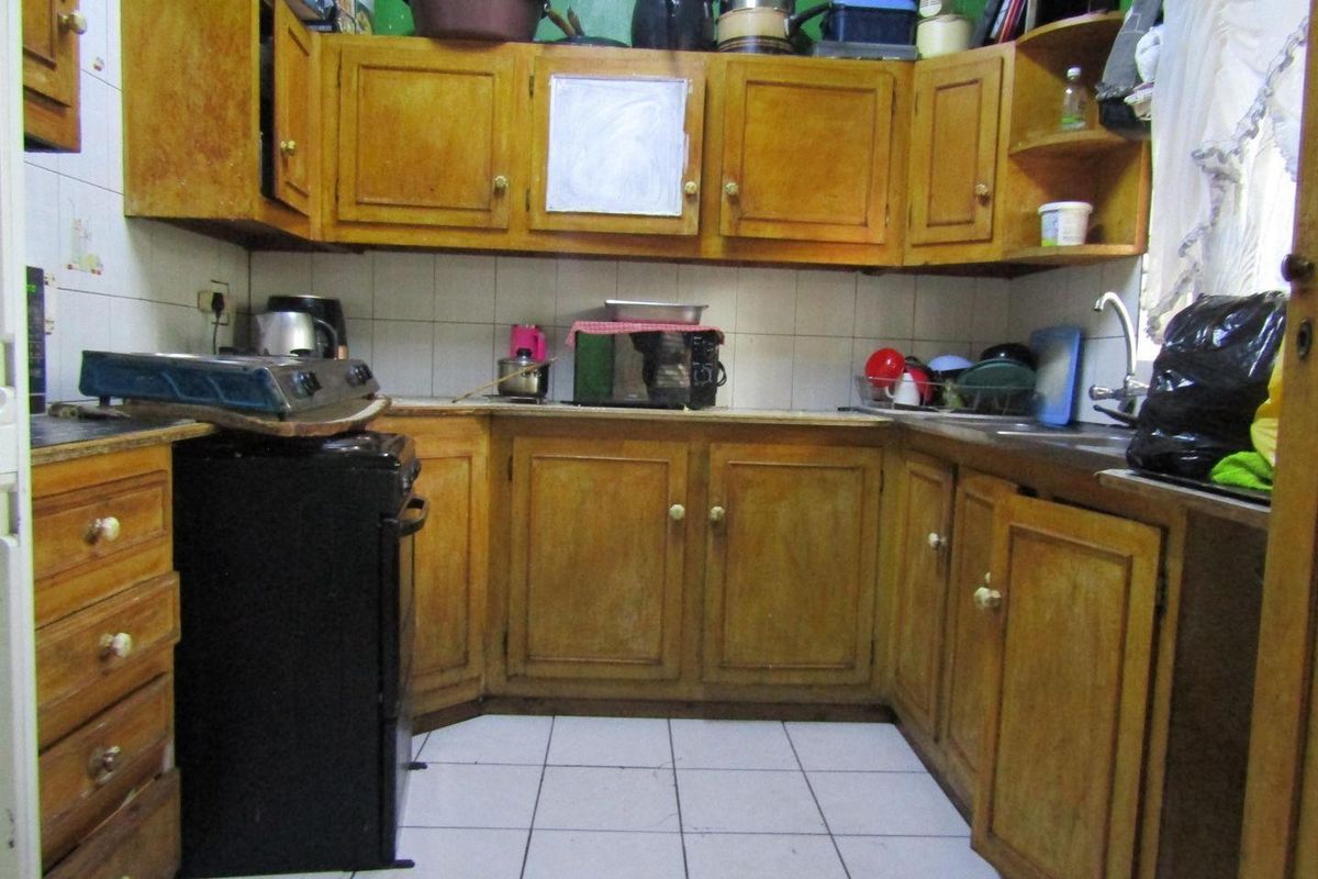 A dated kitchen featuring wooden cabinetry, tiled backsplash, and tiled flooring, offering potential for modernization and renovation.