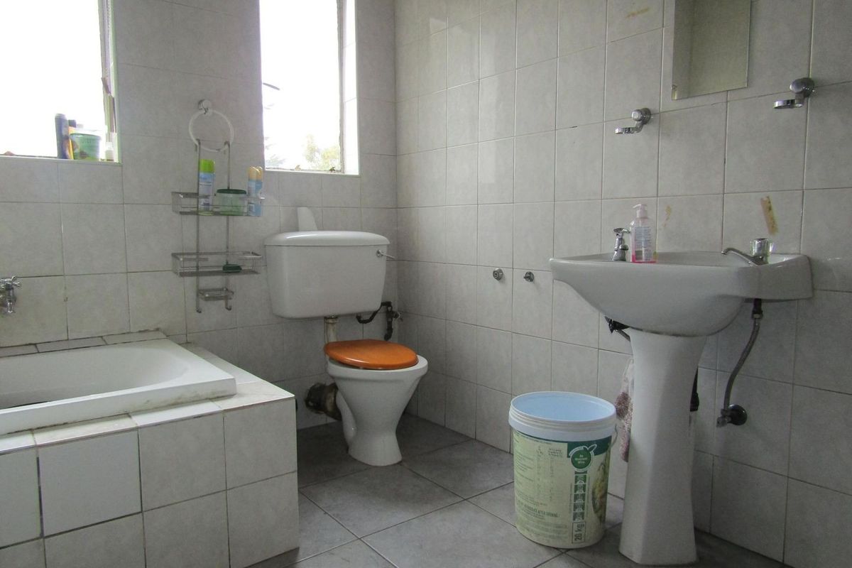 A dated bathroom featuring a bathtub, pedestal sink, and toilet with full-height wall tiling and floor tiles.