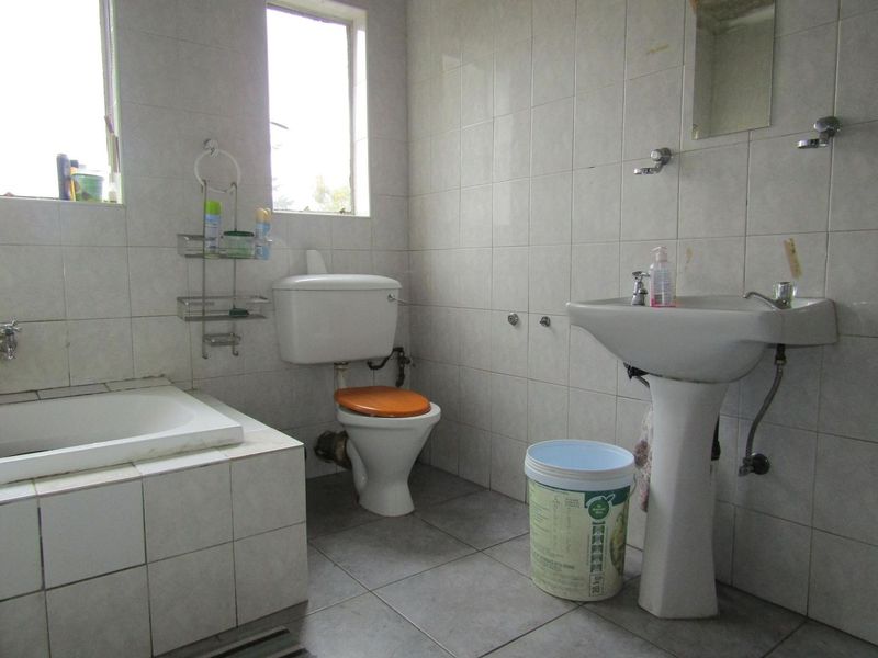 A dated bathroom featuring a bathtub, pedestal sink, and toilet with full-height wall tiling and floor tiles.