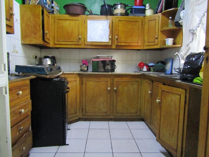 A compact kitchen featuring dated wooden cabinetry, tiled backsplash, and tiled flooring, offering potential for a modern renovation.