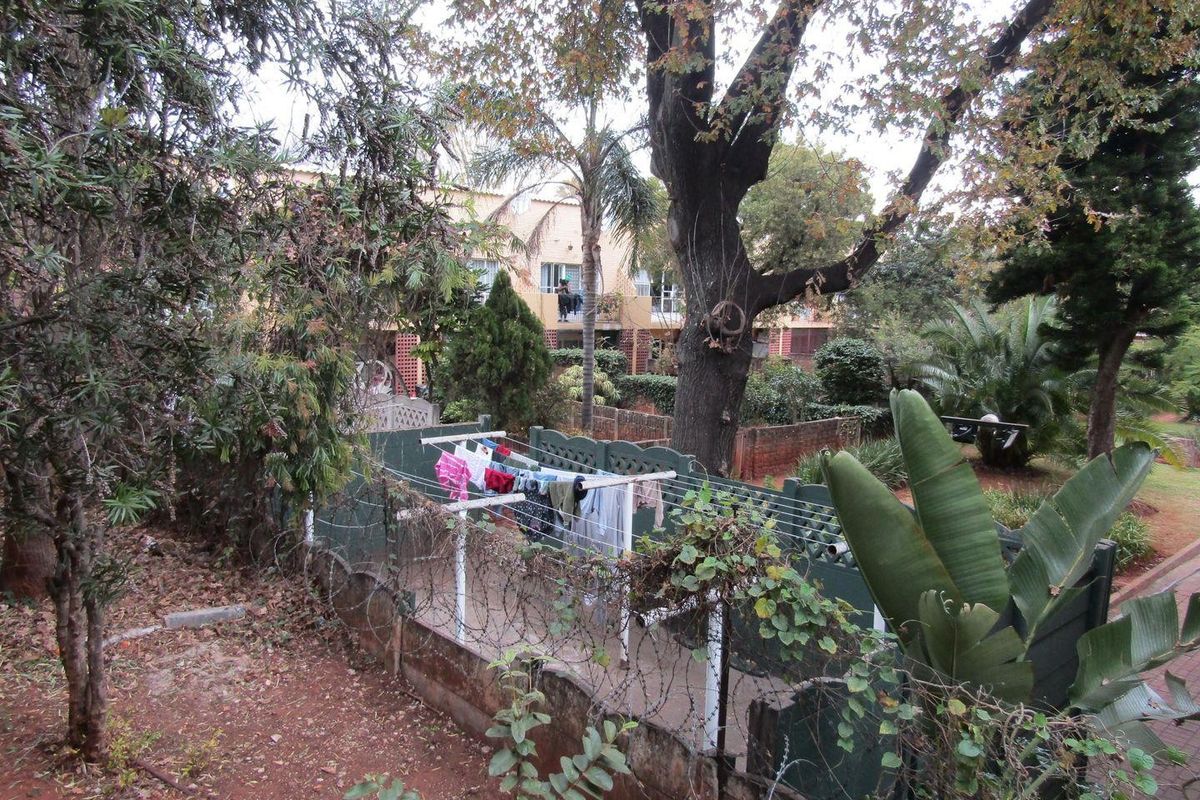 View of the rear garden area featuring mature trees, established landscaping, and a brick boundary wall with security fencing.