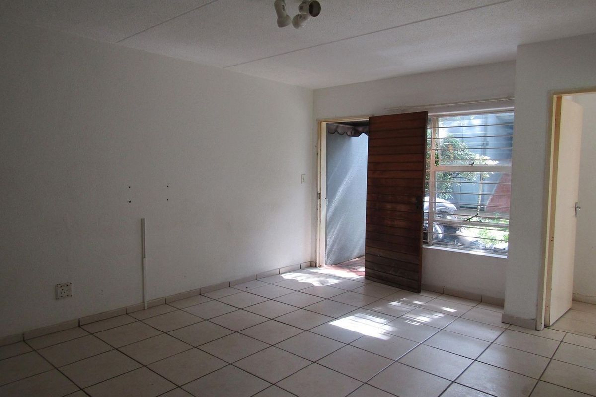 An empty living room featuring ceramic floor tiles, security bars on the window, and direct access to an outdoor area.