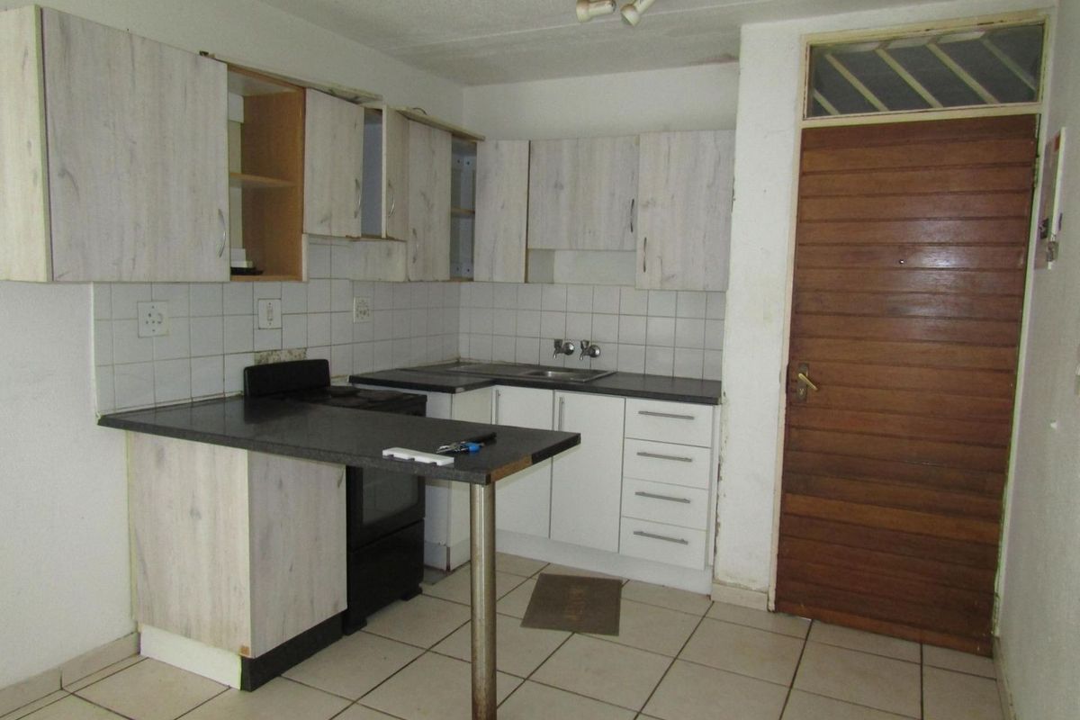 A functional kitchen featuring laminate cabinetry, tiled backsplash, and ceramic flooring, currently requiring cosmetic updates and repairs to cabinet fixtures.