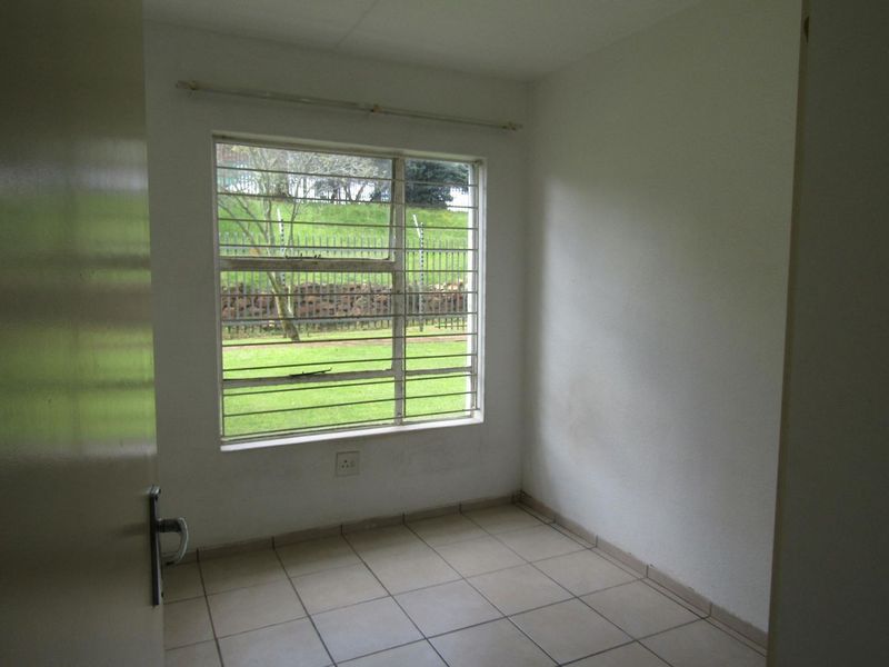 A vacant bedroom featuring tiled flooring, a window with security bars, and neutral wall finishes, offering a blank canvas for personalization.