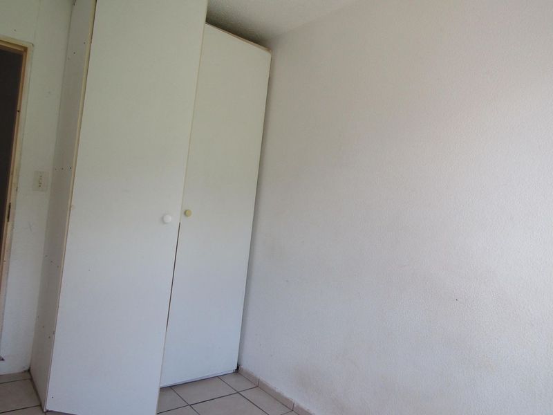 A simple bedroom featuring built-in cupboards and tiled flooring, offering a blank canvas for potential interior updates.
