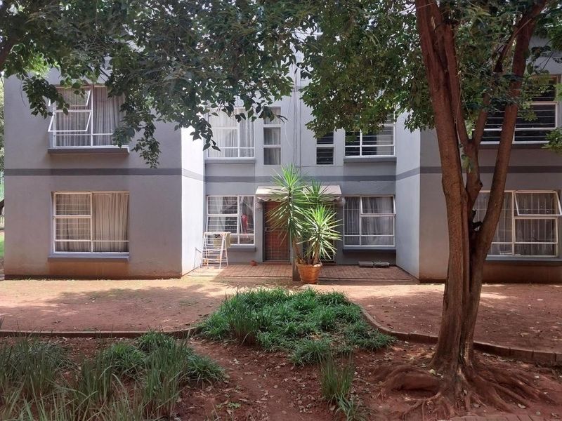 Rear view of a multi-story apartment building featuring aluminium window frames, a paved patio area, and established garden surroundings.