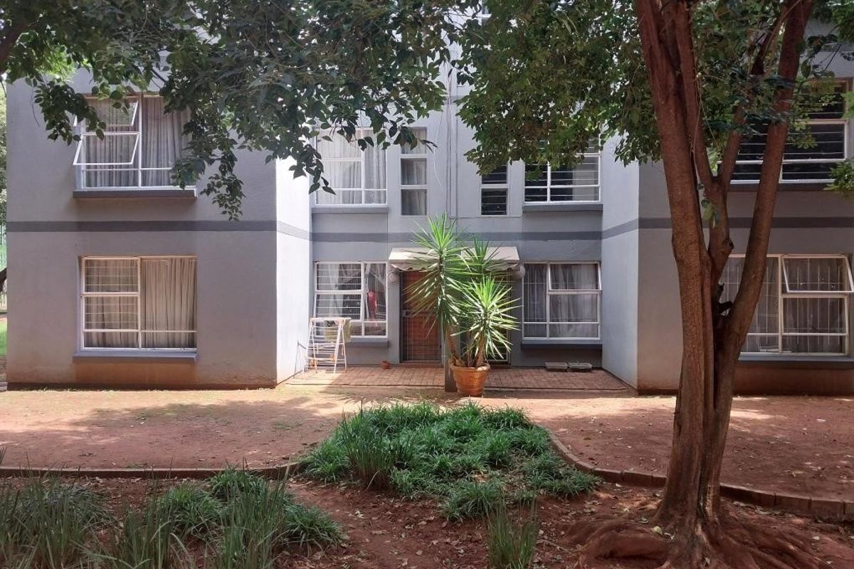 Rear view of a multi-story apartment building featuring aluminium window frames, a paved patio area, and established garden surroundings.