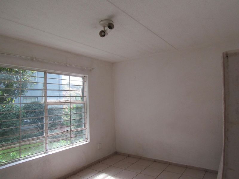 An empty bedroom featuring tiled flooring, security bars on the window, and a ceiling-mounted spotlight fixture.