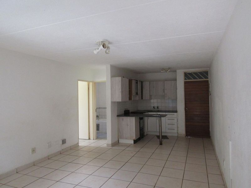Open plan living area featuring tiled flooring and a compact kitchen with built-in cabinetry and integrated appliances.
