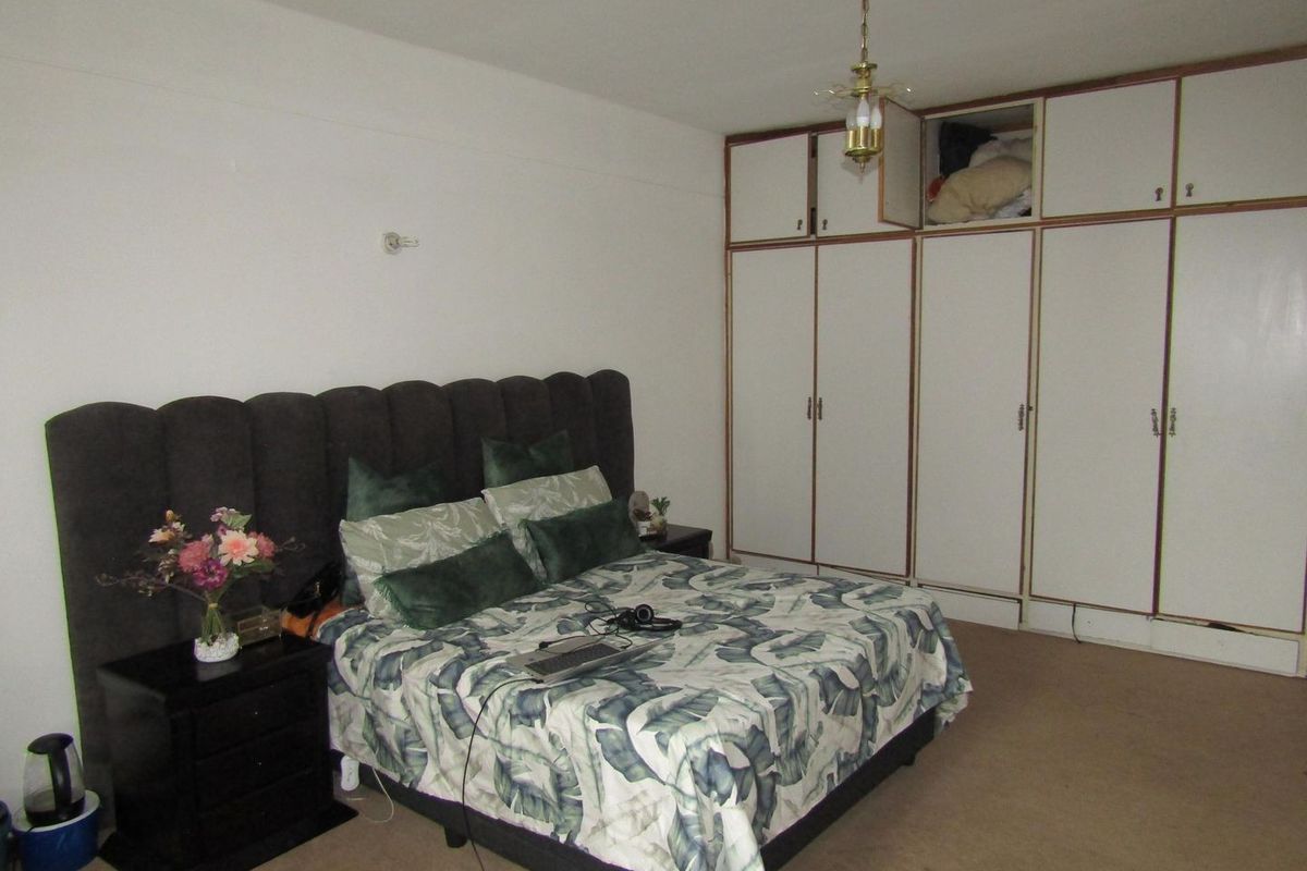 A spacious bedroom featuring extensive built-in cupboards and neutral carpeting, offering a functional layout ready for modern updates.