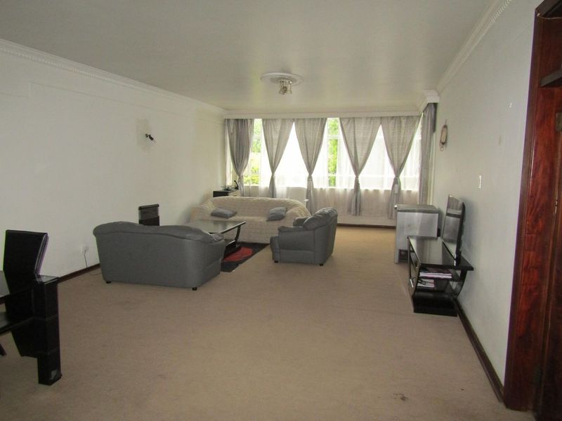 Spacious living room featuring neutral carpeting, decorative ceiling cornices, and large windows allowing for natural light.