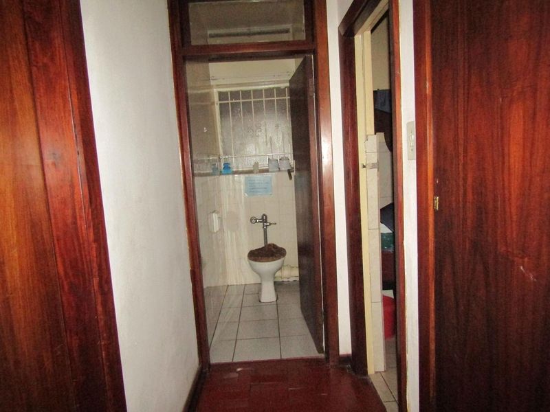 A narrow hallway leading to a bathroom with tiled floors and wooden door frames, showing signs of age and wear.