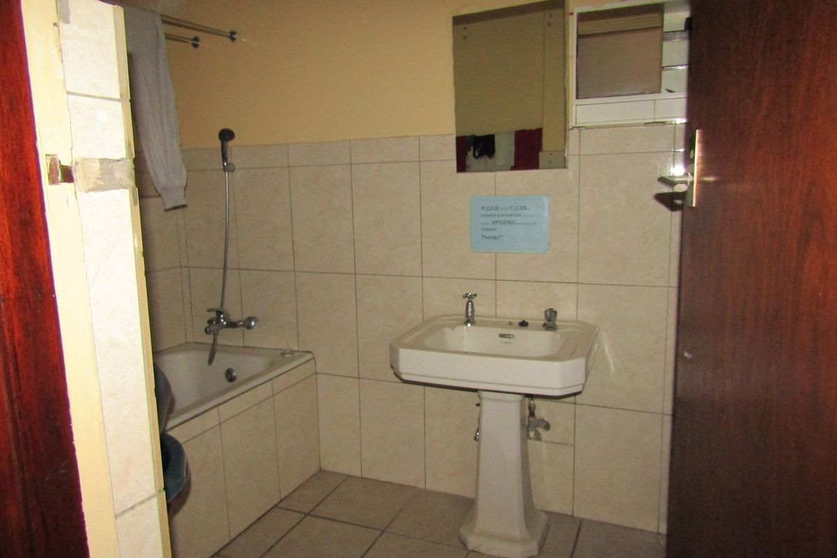 A dated bathroom featuring a pedestal basin, built-in bathtub with shower mixer, and neutral wall and floor tiling.