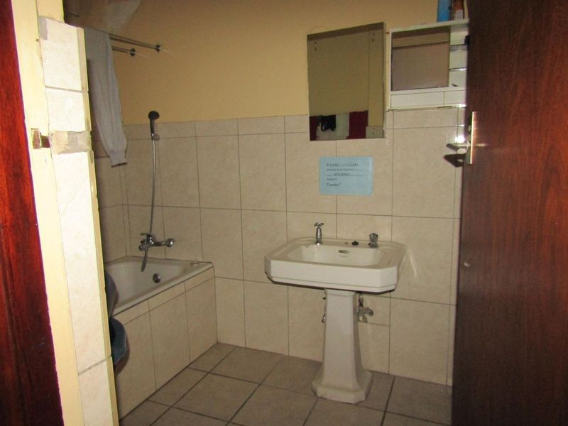 A dated bathroom featuring a pedestal basin, built-in bathtub with shower mixer, and neutral wall and floor tiling.