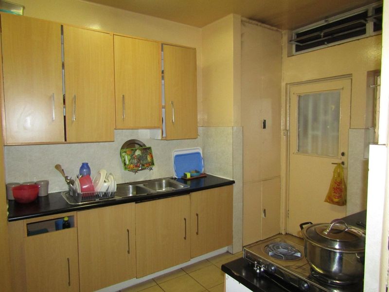 A functional kitchen featuring laminate cabinetry, a double bowl stainless steel sink, tiled backsplash, and a built-in pantry cupboard with direct exterior access.