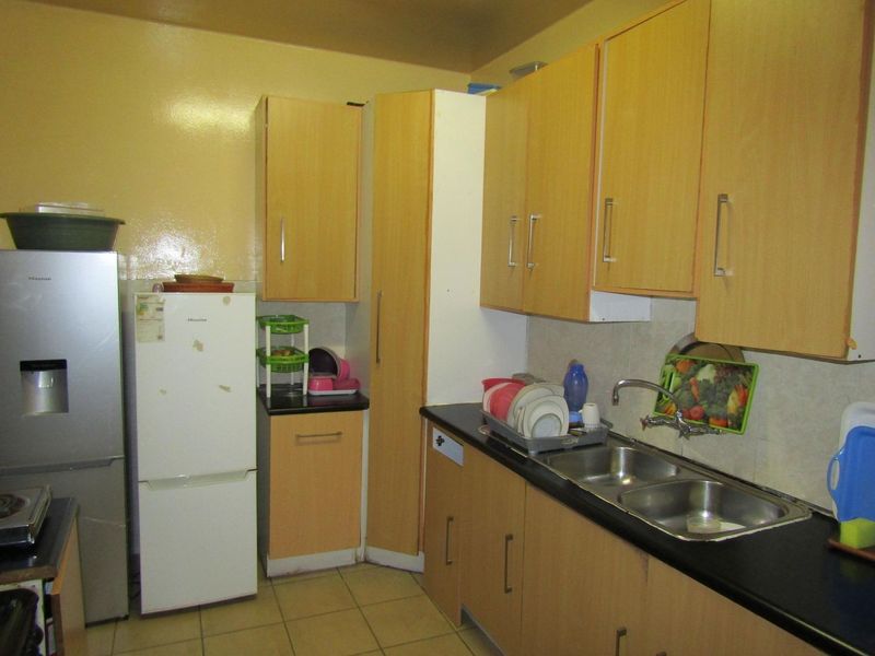 A compact kitchen featuring laminate cabinetry, double bowl stainless steel sink, and tiled flooring, offering a functional layout with potential for modern updates.