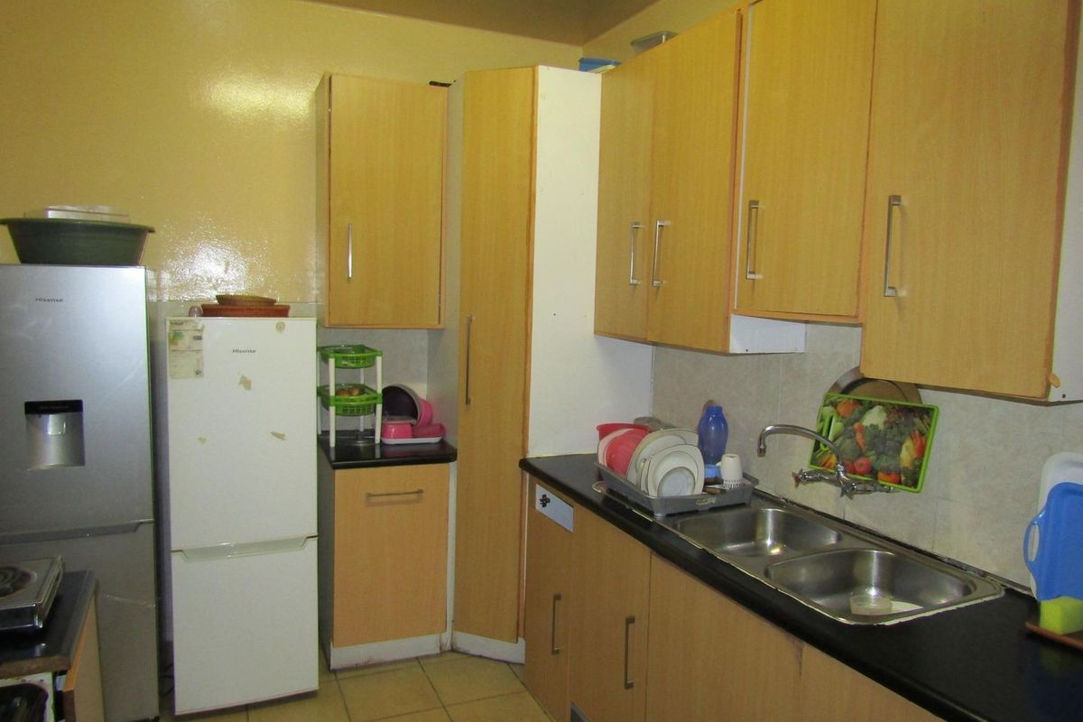 A compact kitchen featuring laminate cabinetry, double bowl stainless steel sink, and tiled flooring, offering a functional layout with potential for modern updates.