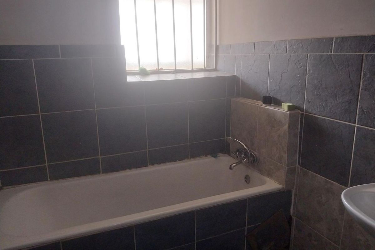 A functional bathroom featuring a bathtub with a mixer tap, tiled wall finishes, and a window with security bars.