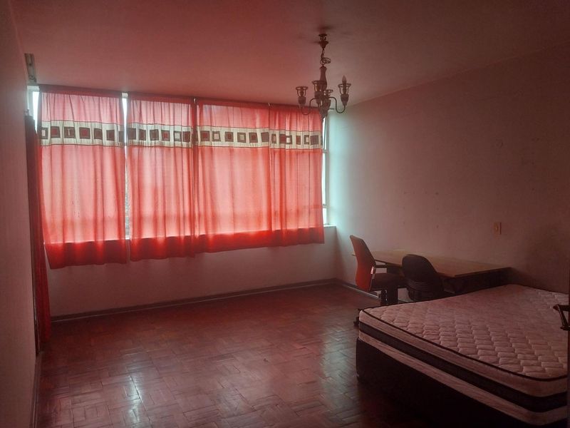 A bedroom featuring parquet flooring, a ceiling chandelier, and a large window with red curtains.