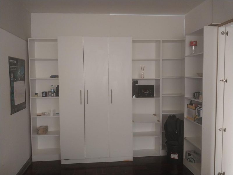 A bedroom featuring extensive white built-in cabinetry and open shelving units, providing ample storage space with dark hardwood flooring.
