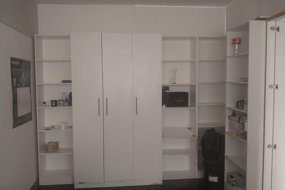 A bedroom featuring extensive white built-in cabinetry and open shelving units, providing ample storage space with dark hardwood flooring.