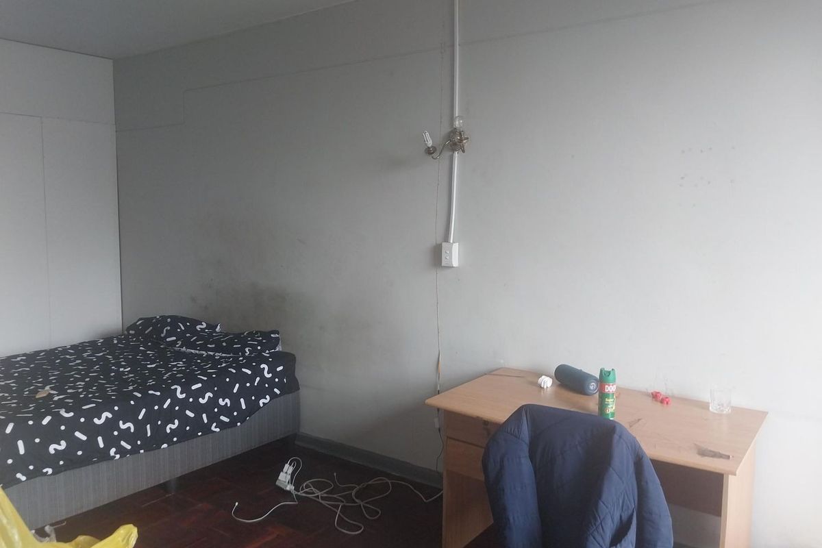 A bedroom featuring parquet flooring and wall-mounted lighting with visible surface-mounted electrical conduit and wall staining.