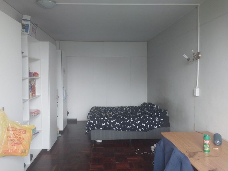 A bedroom featuring dark parquet flooring and built-in storage cupboards, requiring cosmetic updates to the wall finishes and lighting.