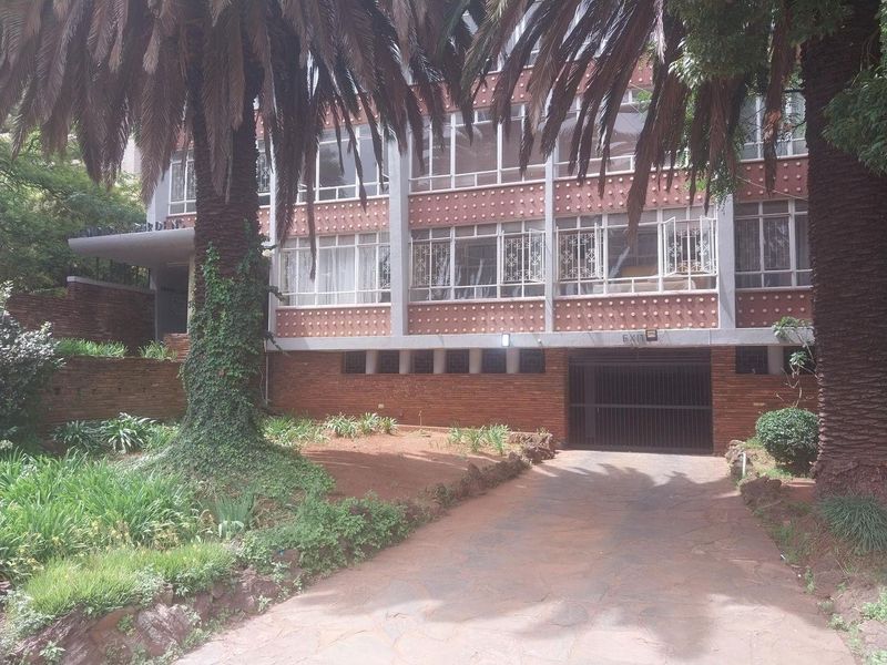 Front elevation of a multi-story apartment building featuring brick facade, paved driveway, and secure garage access with mature landscaping.