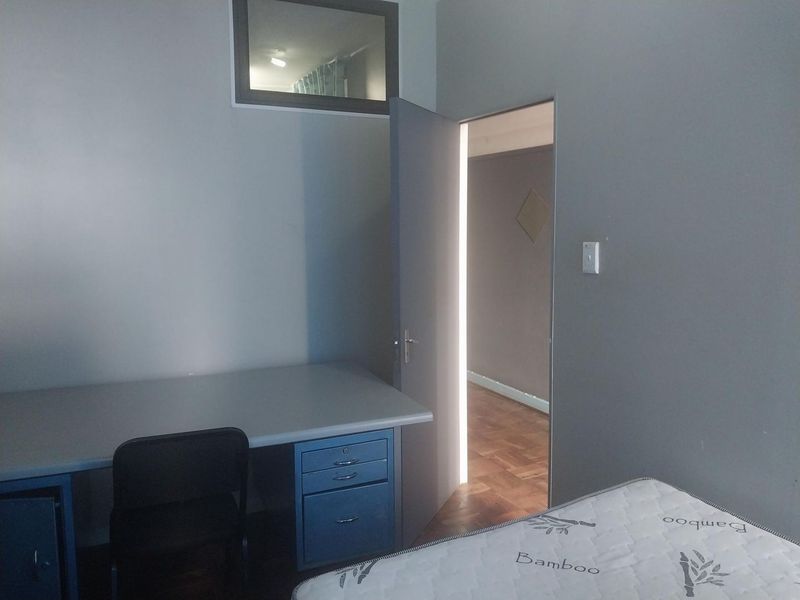 A bedroom featuring a built-in desk, a transom window, and an open doorway leading to an adjacent room with parquet flooring.