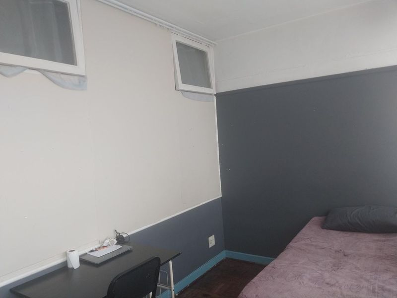 A bedroom featuring parquet flooring and high-level windows, currently requiring cosmetic updates to the wall finishes and trim.